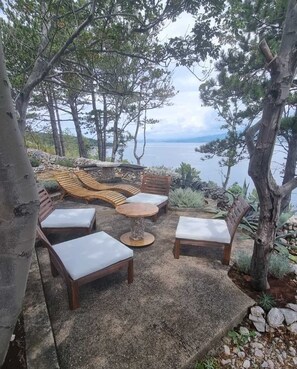 Un patio con sillones de madera y una mesa redonda, con vista a un cuerpo de agua.