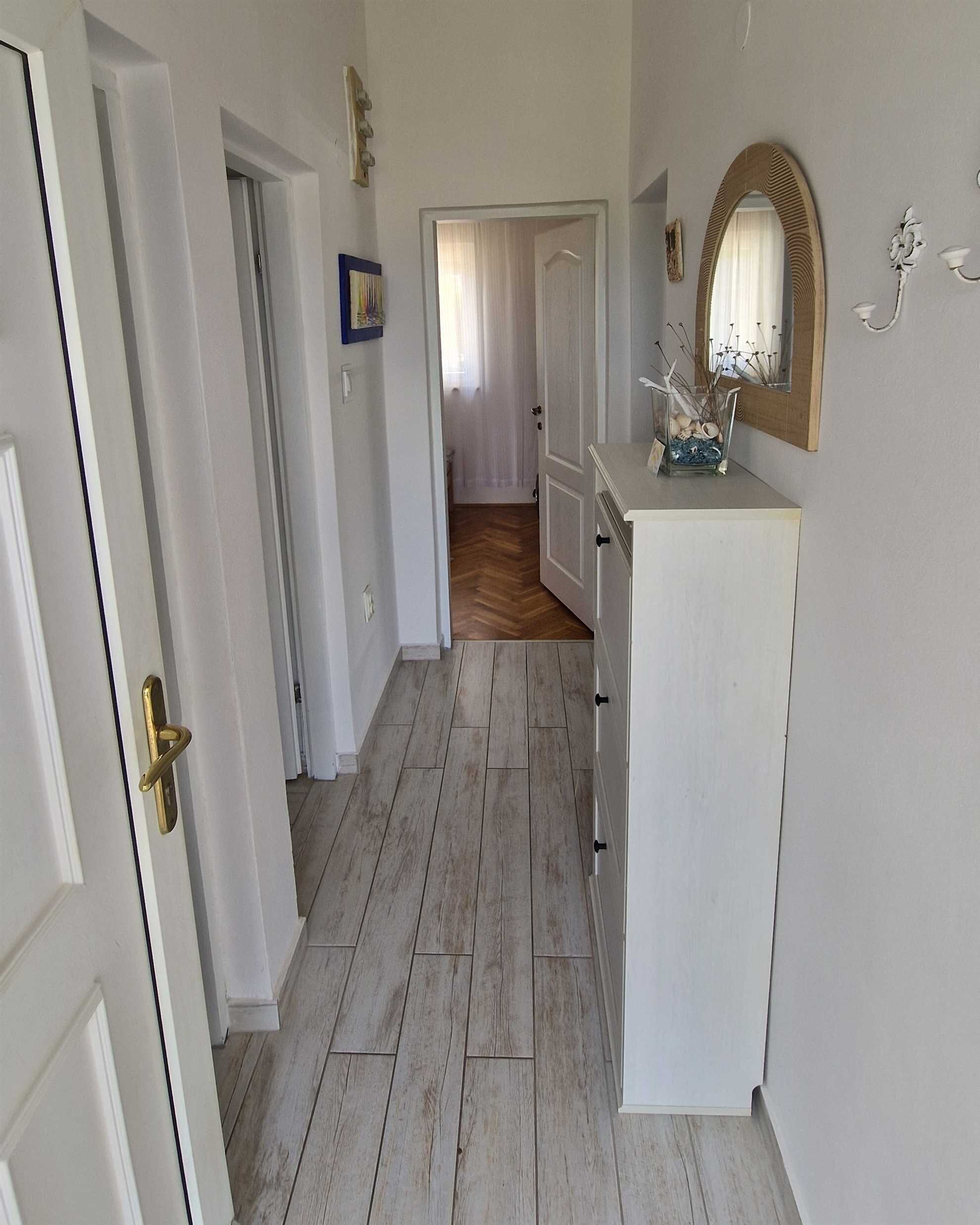 Un couloir doté d’un plancher en bois, de murs blancs et d’une armoire blanche avec un miroir.
