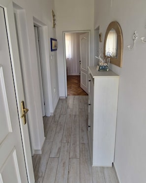 A hallway with wooden flooring, white walls, and a white cabinet with a mirror.