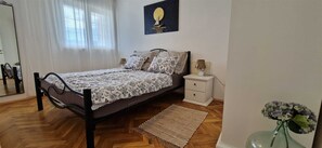 A bedroom with a bed, bedside table, nightstand, and a wall-mounted artwork.