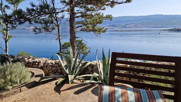 A bench with a striped cushion, a stone wall, and a view of a lake with mountains in the background.