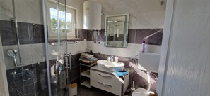 A bathroom with a glass shower enclosure, a sink with a mirror above, and a toilet. - Apartment Sanjug (Silo - island Krk)