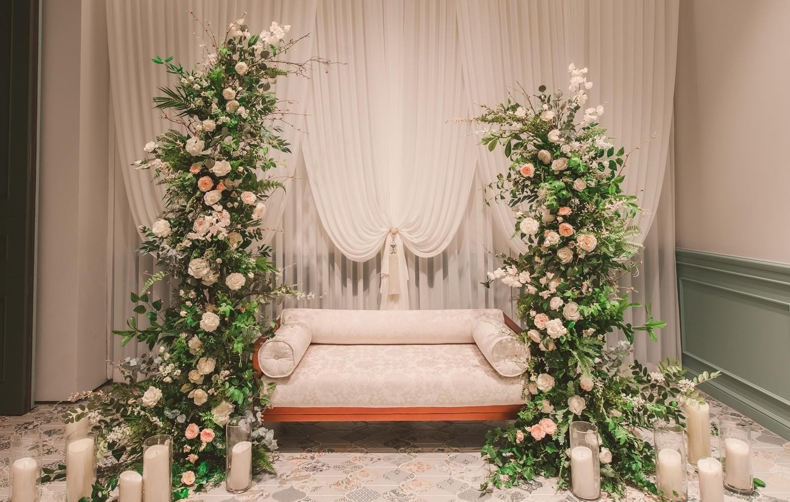 A room with a sofa, floral arrangements, and candles.