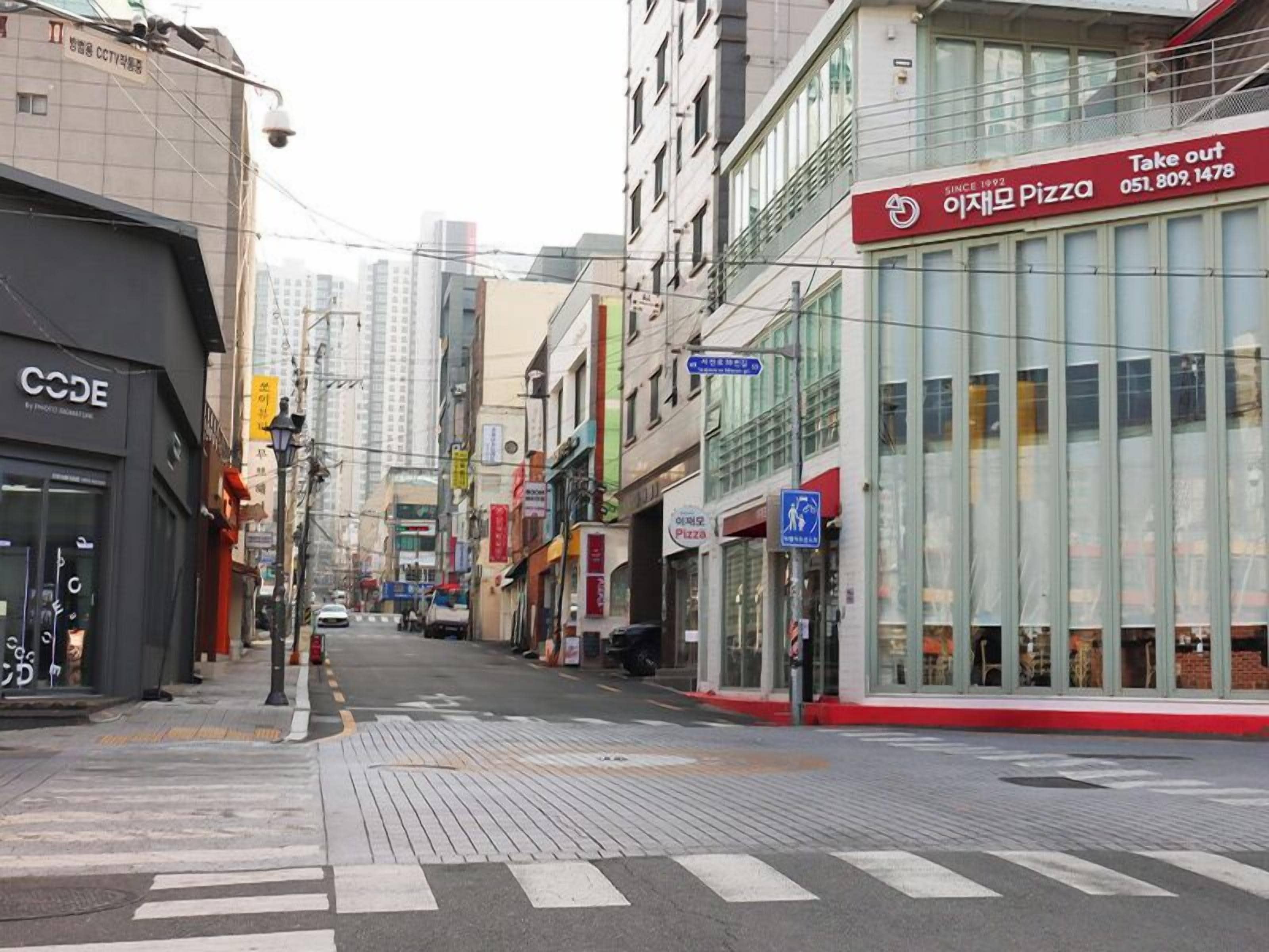 Vista de la calle con una pizzería y una tienda llamada CODE.