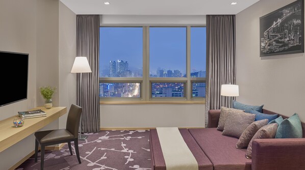 Habitación de hotel con vista a la ciudad, escritorio, sofá y televisor.