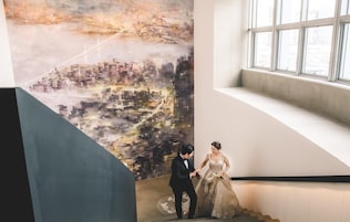 Una pareja en una escalera con un mural de un paisaje urbano de fondo.