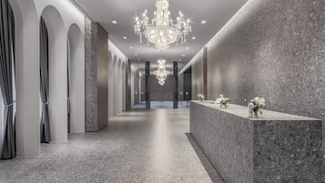 Un moderno vestíbulo de hotel con una gran araña, paredes de mármol y un mostrador de recepción con arreglos florales.