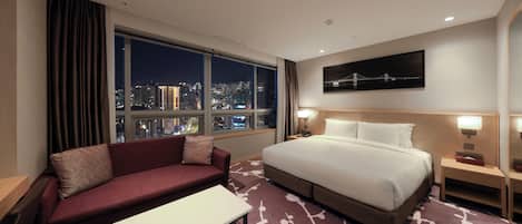 A hotel room with a large bed, a sofa, a coffee table, and a view of the city at night.