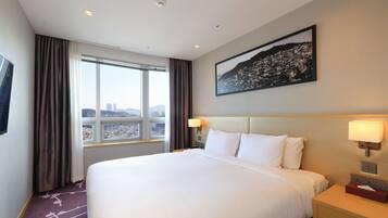 A hotel room with a large bed, two bedside lamps, a nightstand, a window with curtains, and a cityscape view.