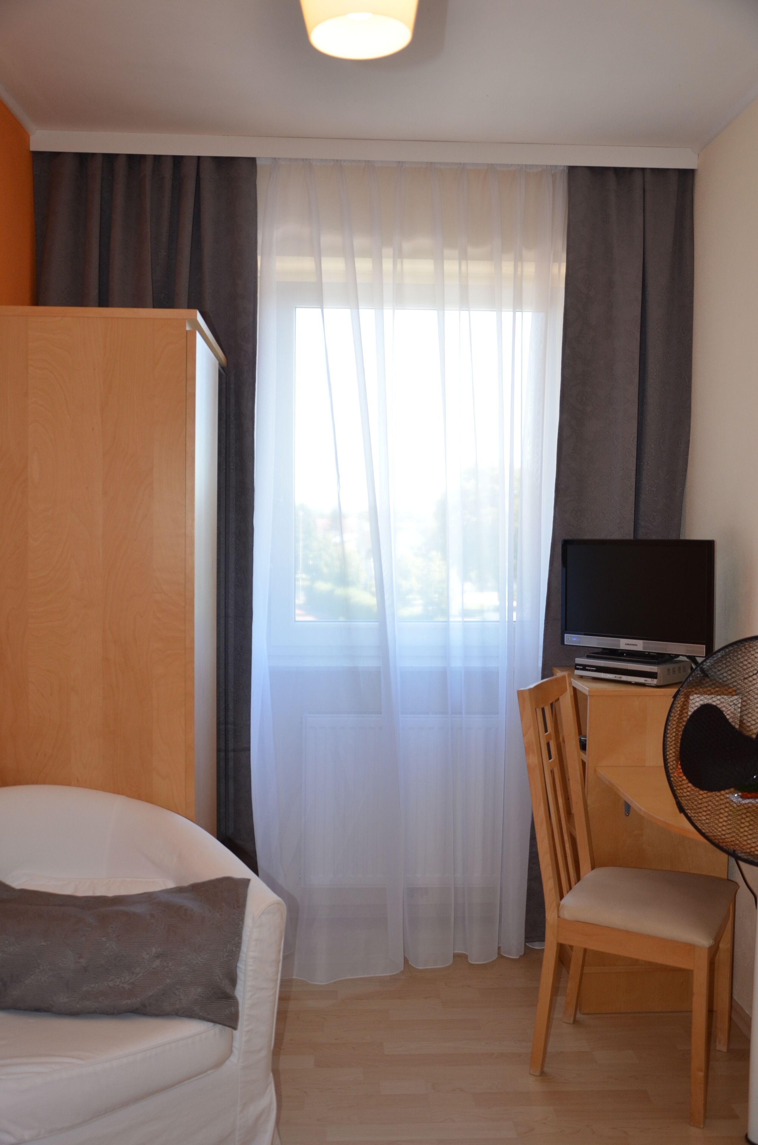 A hotel room with a bed, a desk with a television, a chair, and a wardrobe.