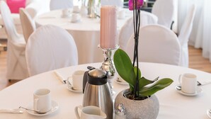 A round dining table with white chairs, a coffee pot, salt and pepper shakers, and a potted orchid.