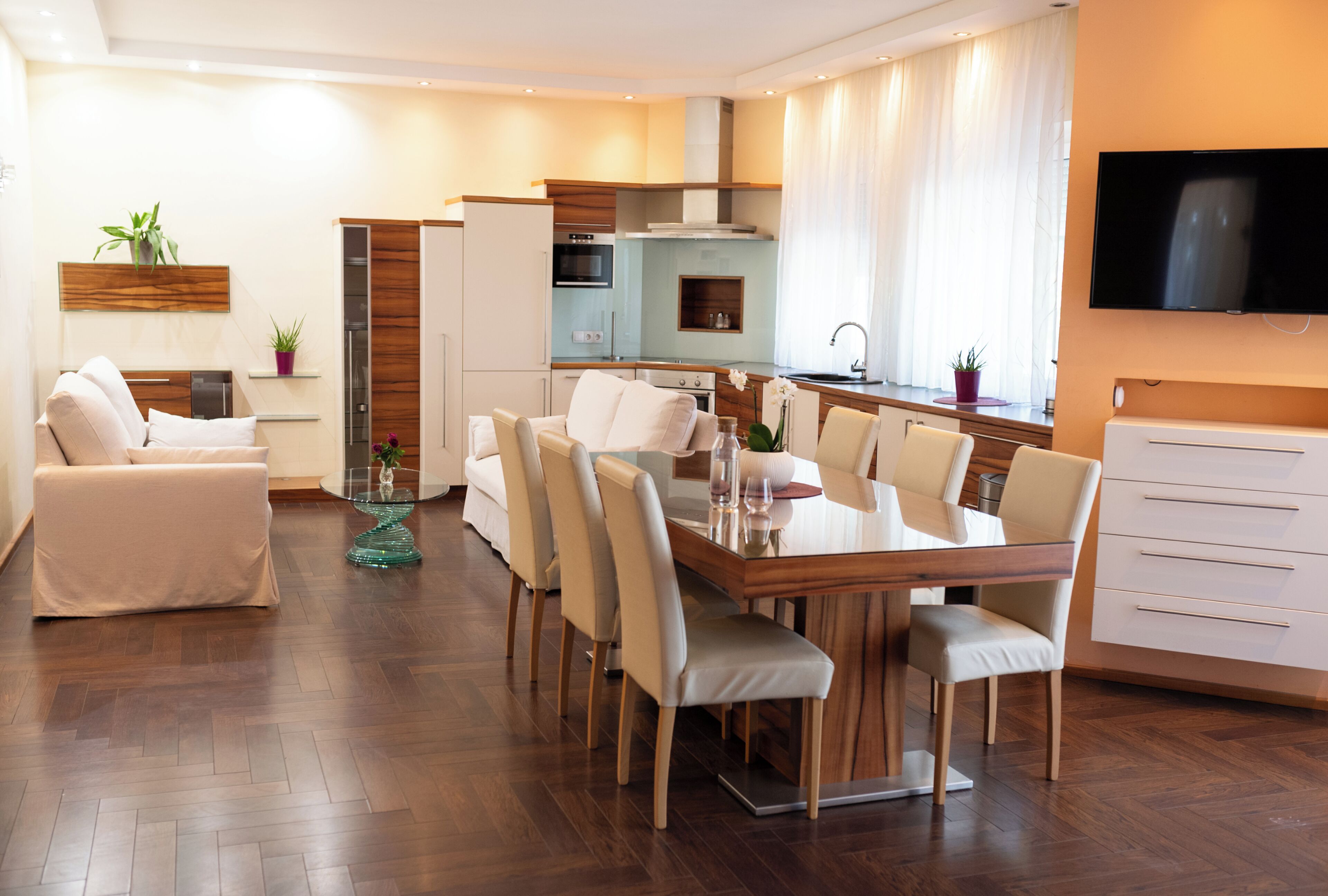 A modern living room with a dining area, kitchen, and a TV mounted on the wall.