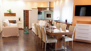A modern living room with a dining area, kitchen, and a TV mounted on the wall.