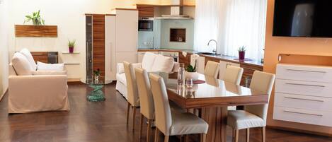 Una sala de estar moderna con comedor, cocina y televisor montado en la pared.