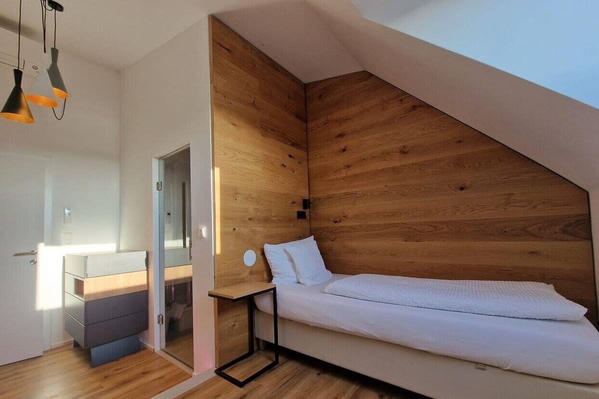 Un dormitorio moderno con techo inclinado, paneles de madera, una cama, mesita de noche y armario.