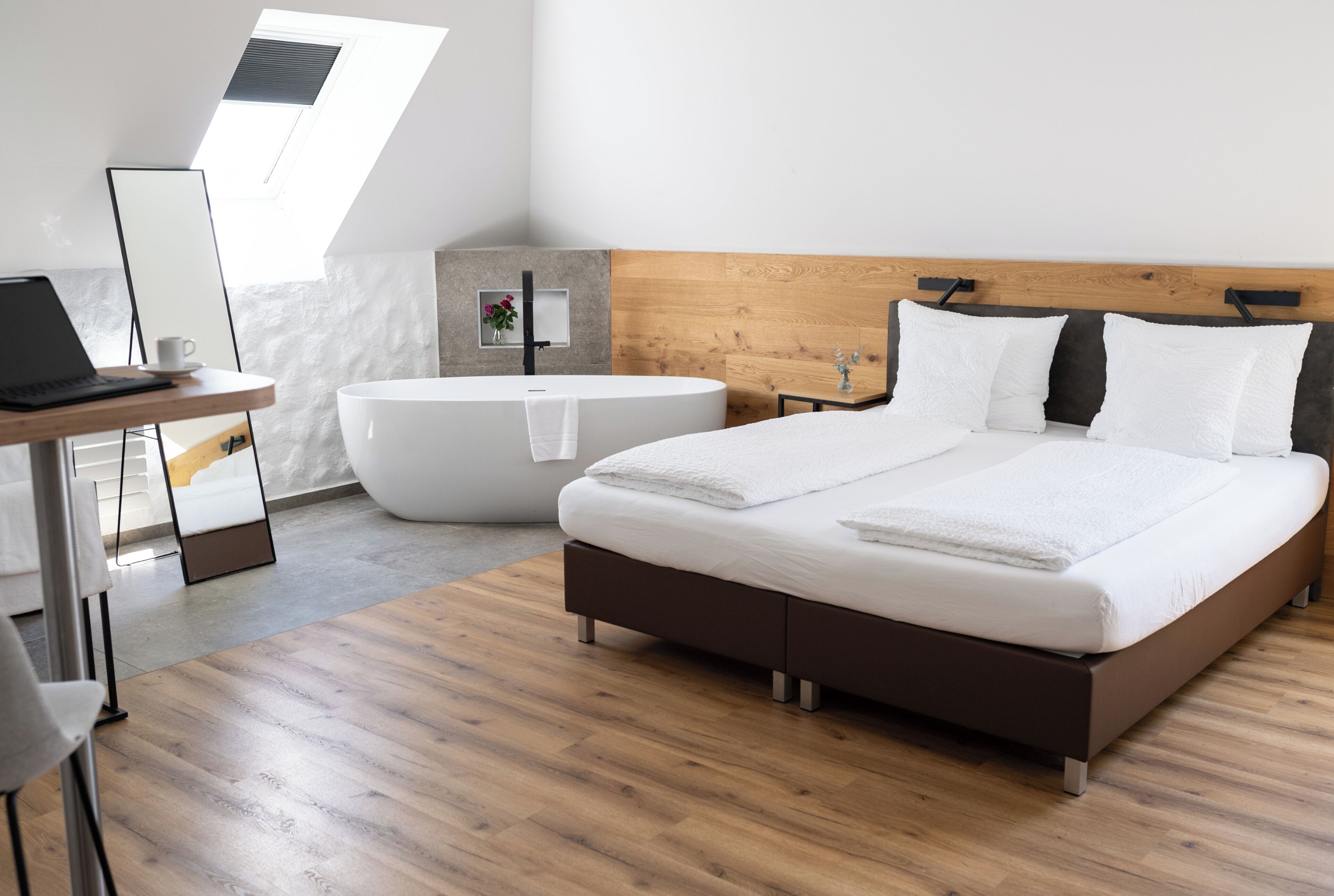 Un dormitorio moderno con una cama grande, una bañera, un escritorio con una computadora portátil y un tragaluz.
