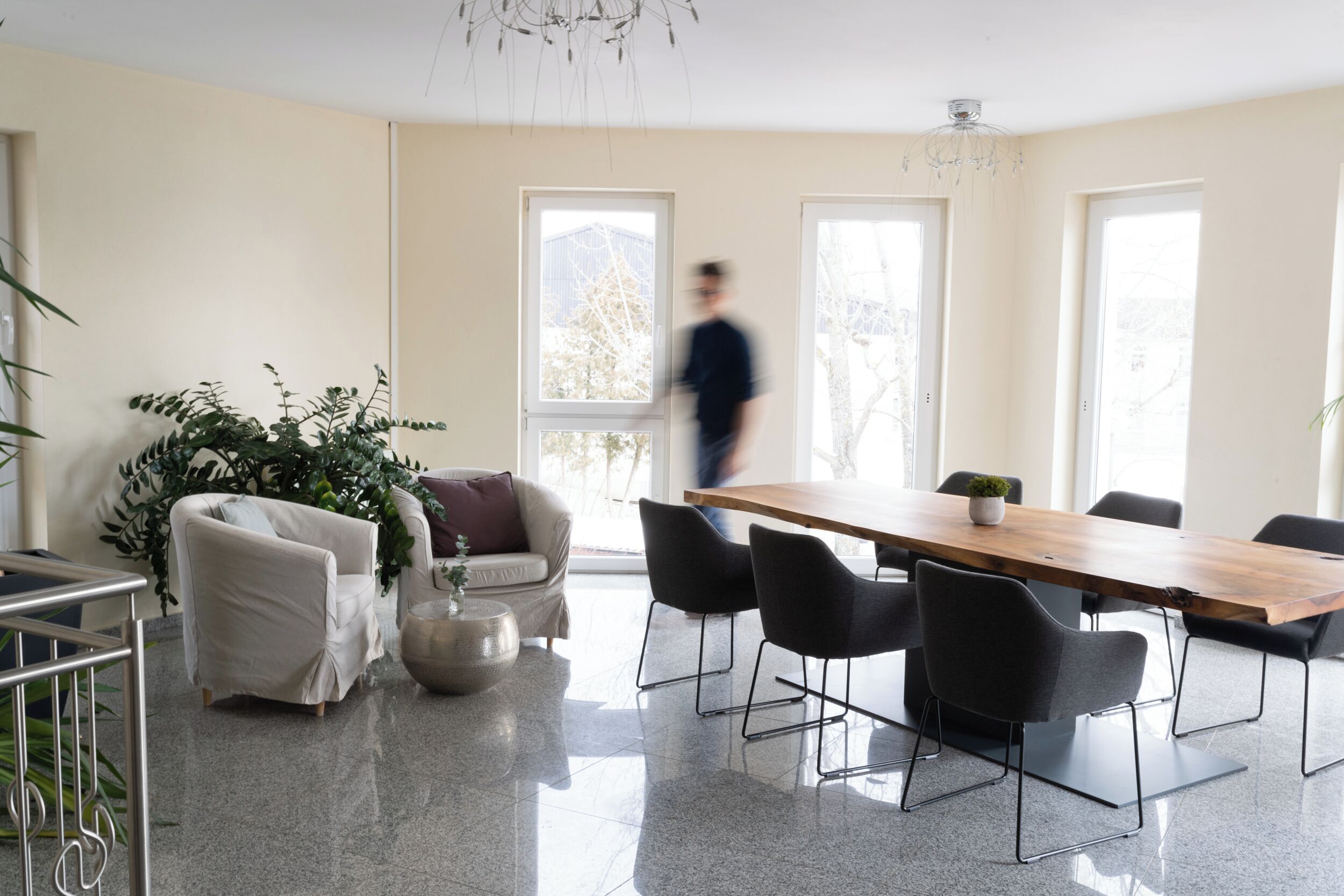 Una sala de reuniones moderna con una larga mesa de madera, sillas negras, un sofá blanco y una planta grande en maceta.