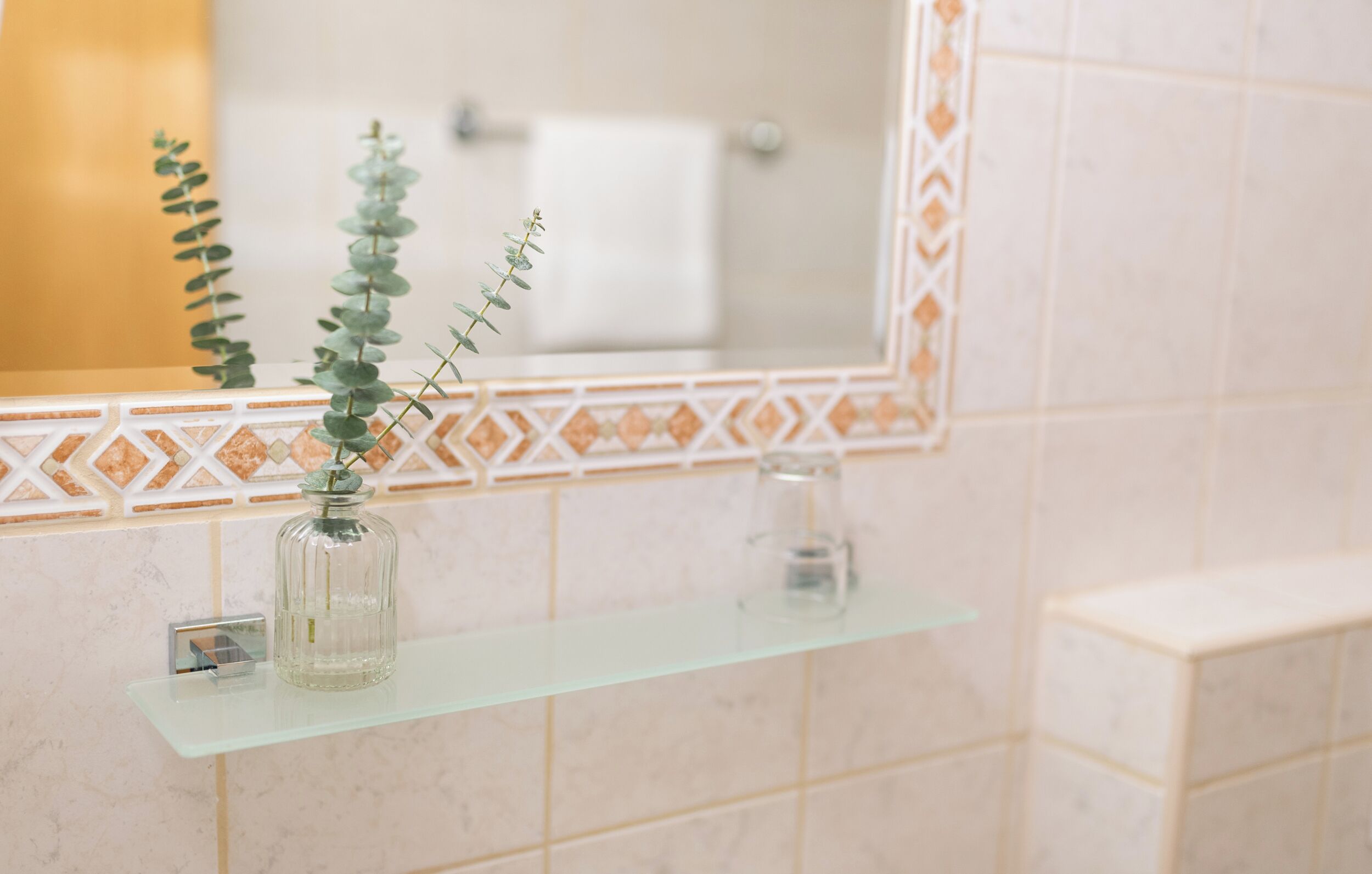 A bathroom with a glass shelf holding a glass jar and a plant.