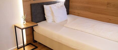 Una cama individual con cabecera, una mesita de noche con lámpara y una planta pequeña.