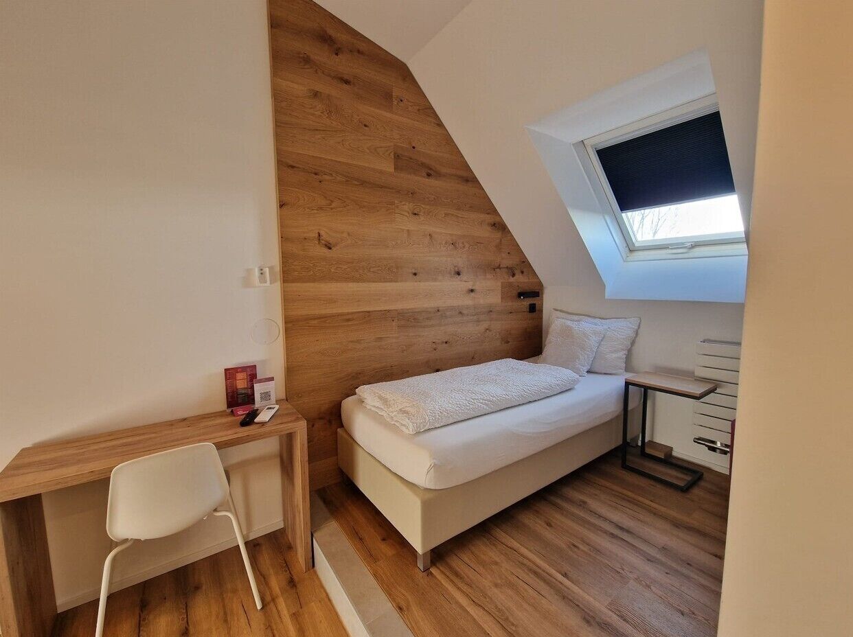 Une petite chambre à coucher moderne avec un plafond en pente en bois, un lit simple, un bureau et une chaise.