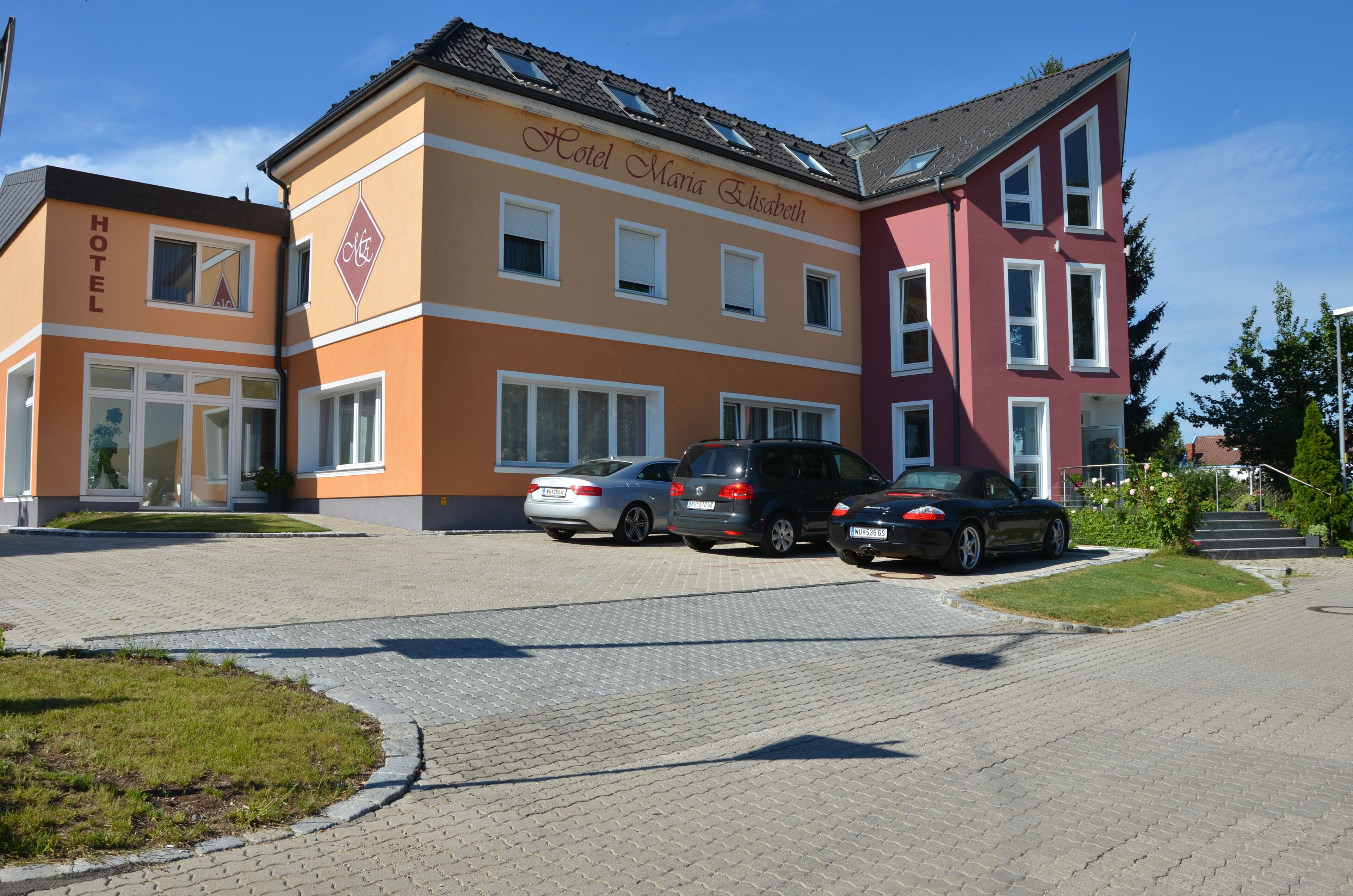 A hotel with a name sign, multiple parked cars, and a paved driveway.