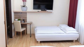 Une chambre d’hôtel comprenant un lit, un bureau avec une chaise, un téléviseur fixé au mur et une plante en pot.