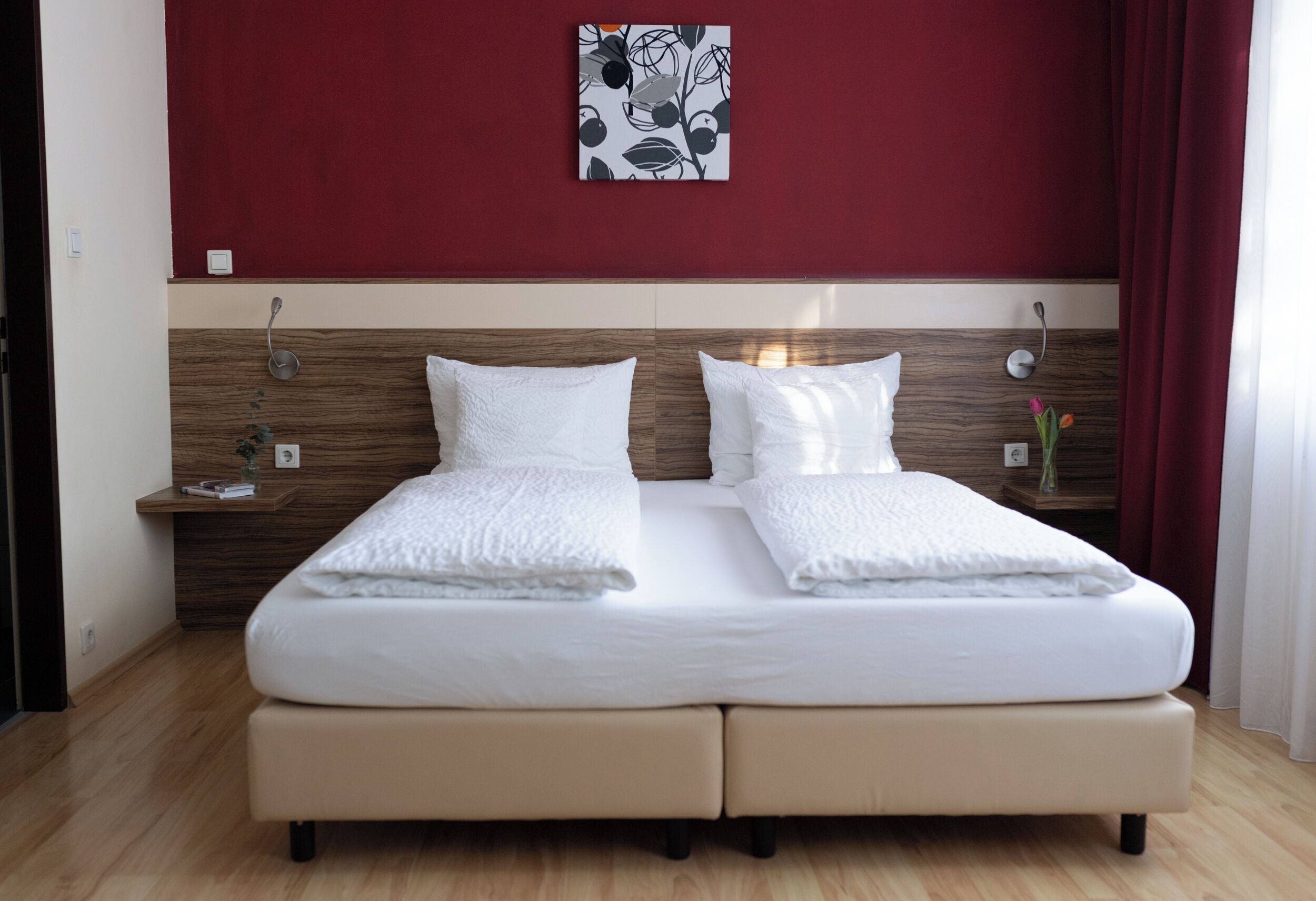 A double bed with white linens, a wooden headboard, and a red accent wall.