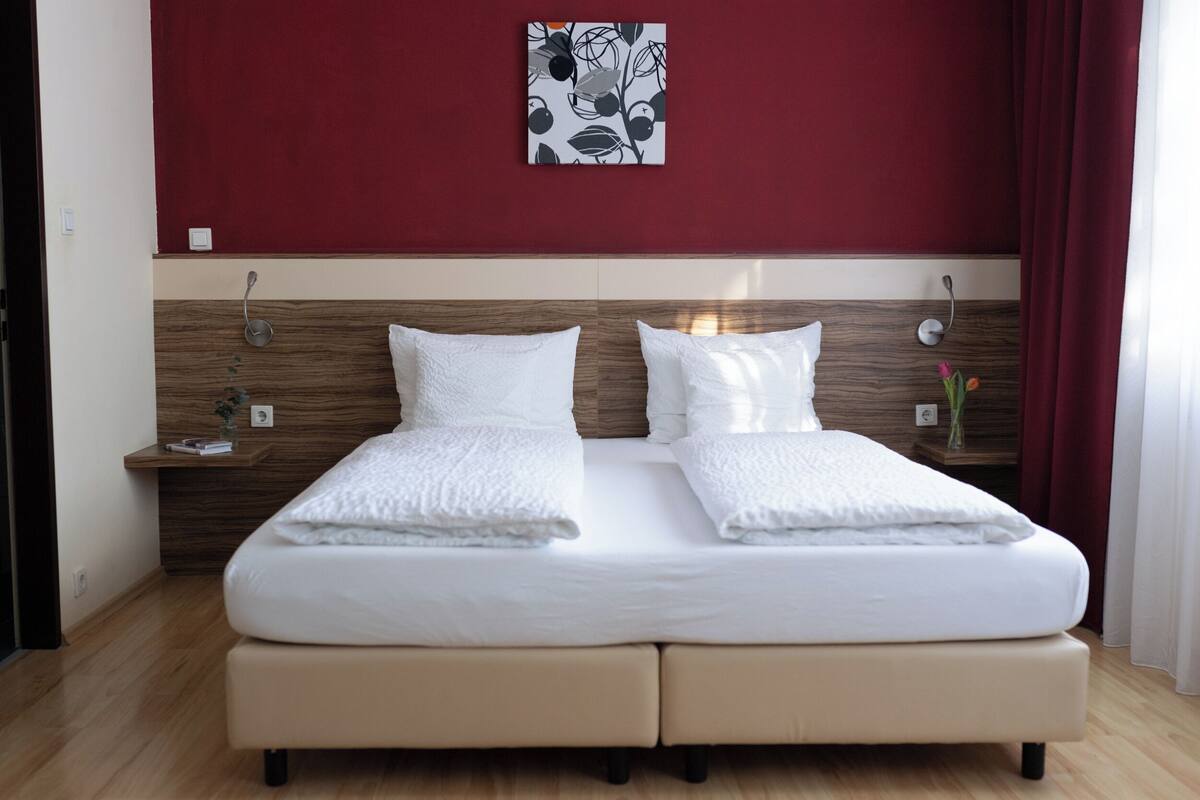 Una cama doble con ropa de cama blanca, un cabecero de madera y una pared de acento roja.