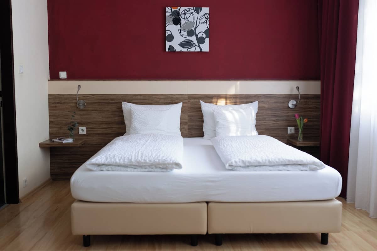Ein Doppelbett mit weißen Bettwäsche, einem hölzernen Kopfteil und einer roten Wand.