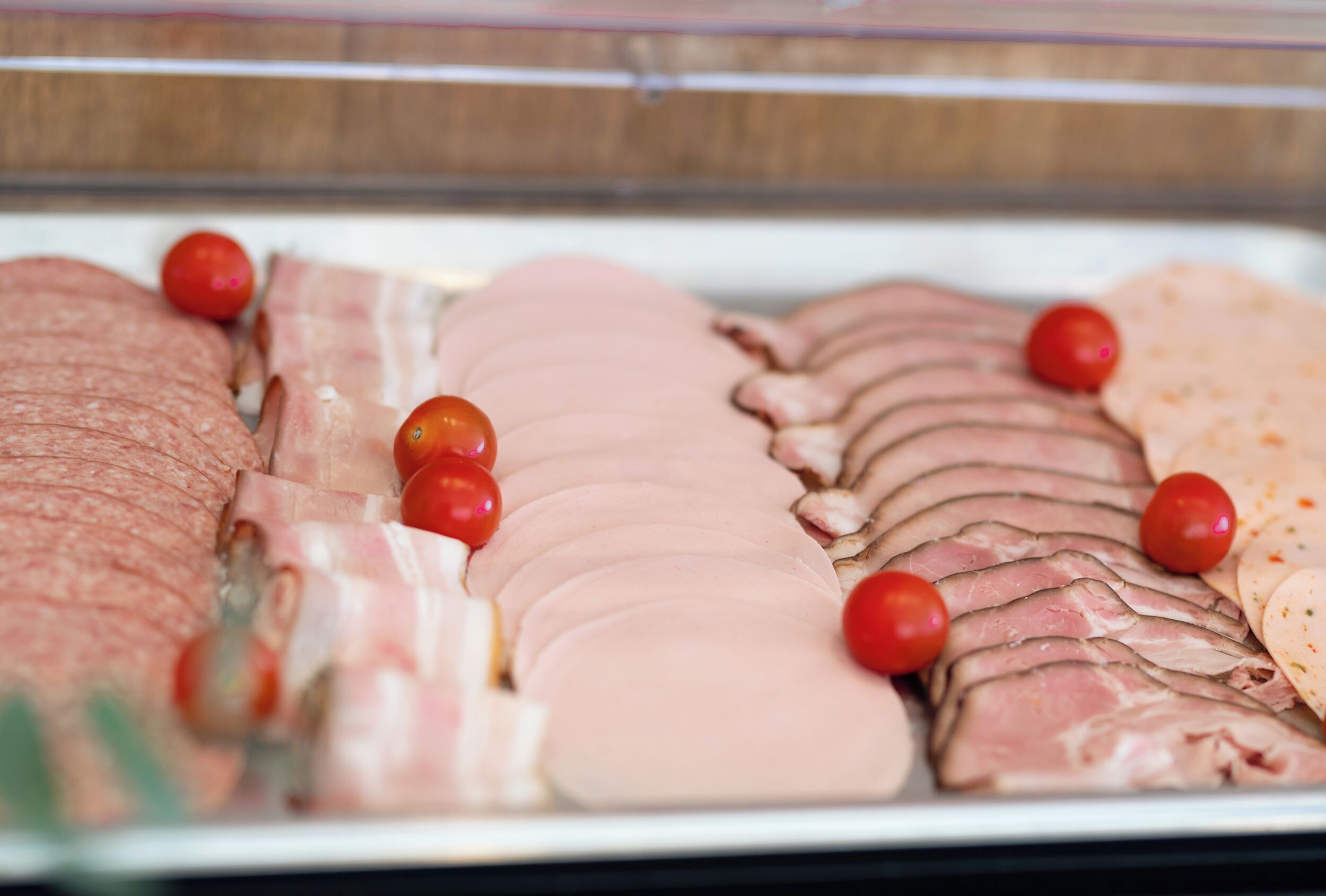 A display of sliced meats and tomatoes in a refrigerated case.