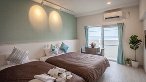 Habitación de hotel con dos camas, balcón con vistas, aire acondicionado y una planta en maceta.
