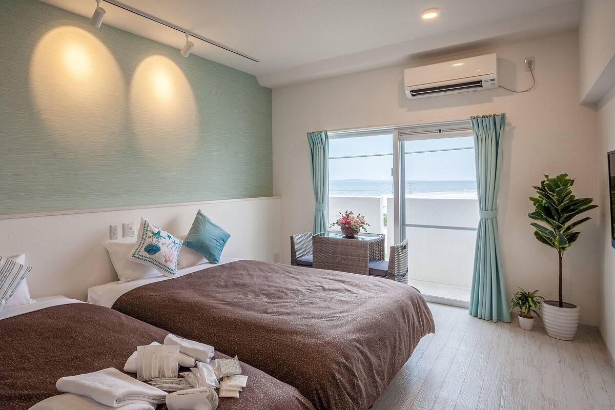 Ein Hotelzimmer mit zwei Betten, einem Balkon mit Blick und einer Klimaanlage, sowie einem Blumentopf.