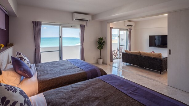 Habitación de hotel con cama, sofá, televisión y vista al mar.