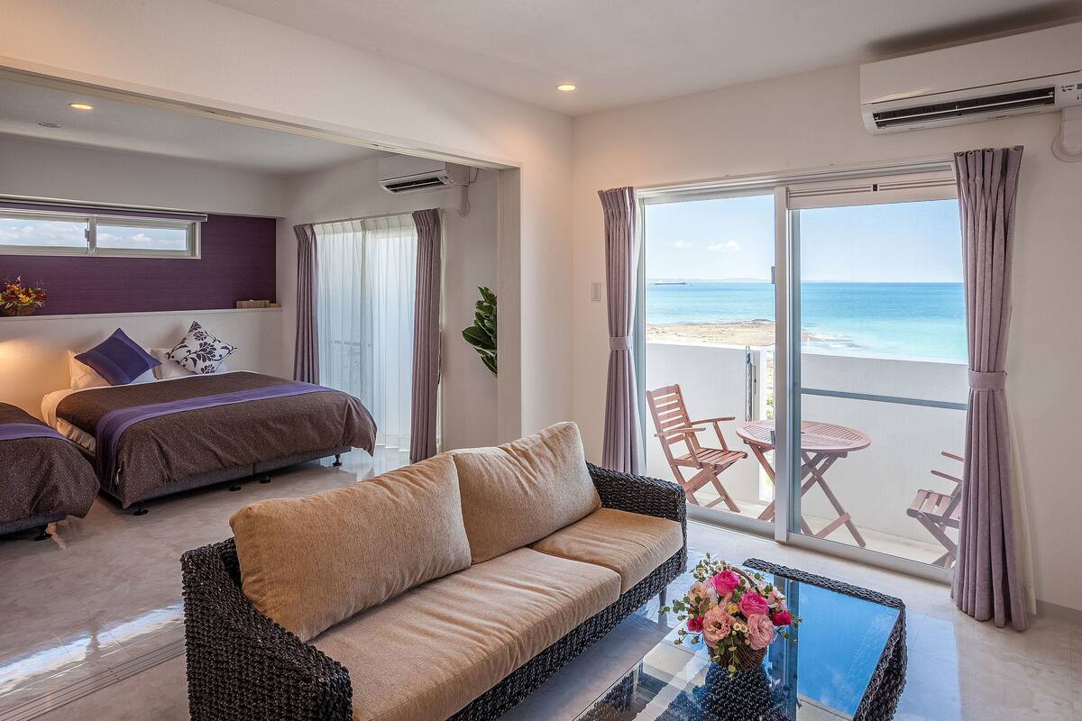 Ein Hotelzimmer mit Bett, einer Couch, einem Balkon mit Tisch und Stühlen sowie Blick auf den Strand.