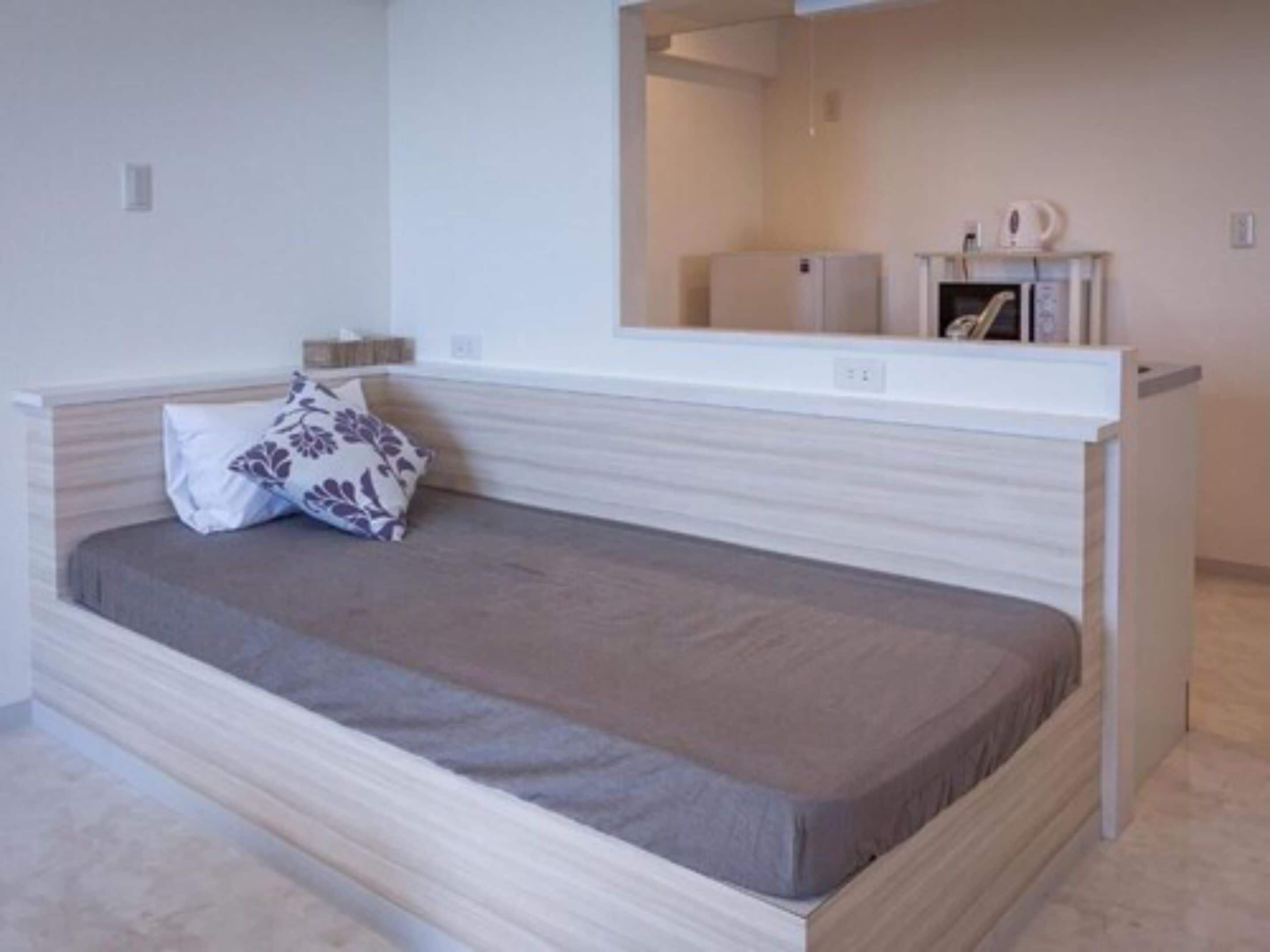 A compact bed with a headboard, a bedside table, and a small cabinet with a microwave.