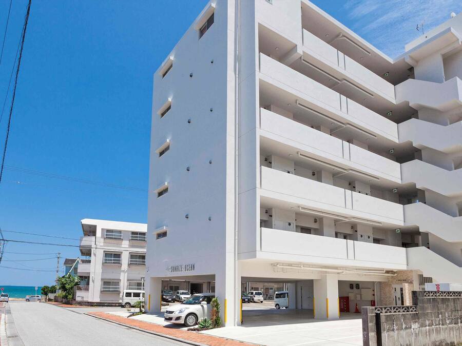 A multi-story building with a parking garage, a sign reading "Sunrise Ocean," and a view of the sea.
