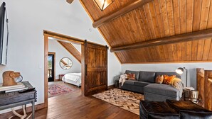 Amplio dormitorio tipo loft con una cama grande, un sofá gris y techo de madera.