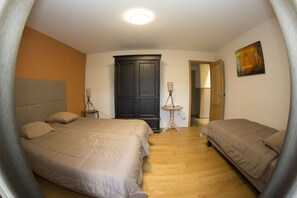 Accommodating multiple guests, this room features a large bed with a headboard and two smaller beds, a wardrobe, and a table with a lamp.