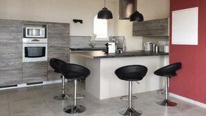 A modern kitchen with built-in appliances, a central island with bar stools, and pendant lighting. - A balcony overlooking the Mediterranean: 20m2 terrace, private parking, bright. (Vence)