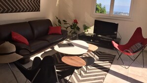A modern living room with a sofa, coffee table, chairs, a TV, and a window with a view. - A balcony overlooking the Mediterranean: 20m2 terrace, private parking, bright. (Vence)