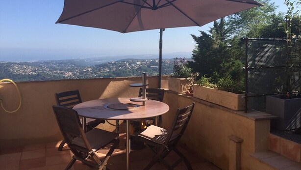 A patio with a table and chairs, an umbrella, and a view of a cityscape. - A balcony overlooking the Mediterranean: 20m2 terrace, private parking, bright. (Vence)