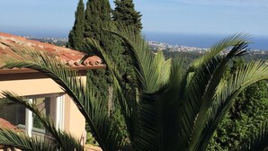A coastal view with a building featuring a tiled roof and palm trees. - A balcony overlooking the Mediterranean: 20m2 terrace, private parking, bright. (Vence)