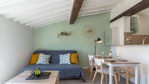 Ein gemütliches Zimmer mit einem Bett, einem Esstisch, Stühlen, einer kleinen Ablage und einer Wanduhr.