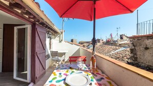 Ein Balkon mit einem roten Sonnenschirm, einem Tisch mit Ananas-Tischdecke und einer Weinflasche.