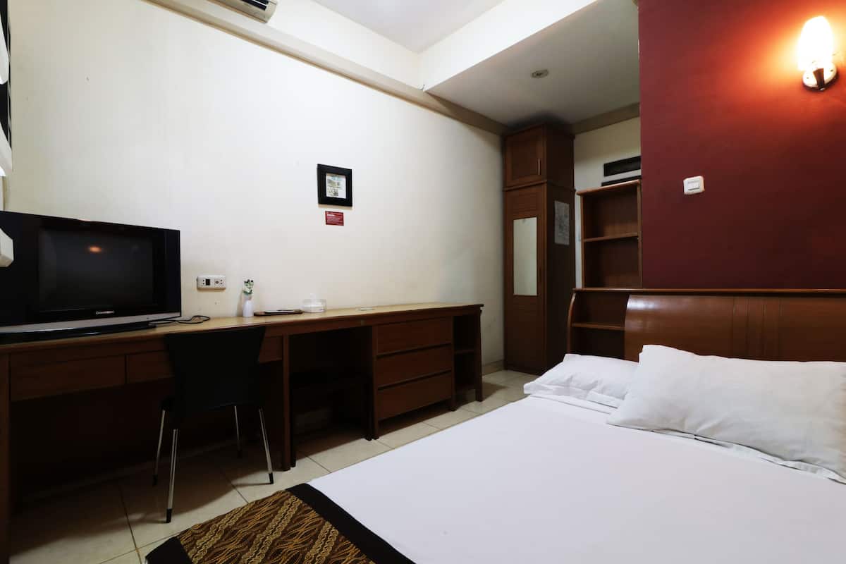 Ein Hotelzimmer mit einem Bett, einem Schreibtisch mit Fernseher, einem Sessel, einem Kleiderschrank und einer Wandleuchte.