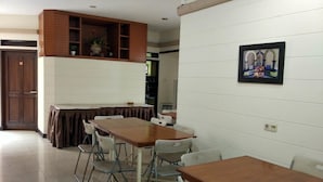A dining area with a long table and multiple chairs, a wooden cabinet above the table, and a framed picture on the wall. - Rumah Tawa Guesthouse 1 (Bandung)