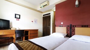 A hotel room with two beds, a desk with a chair, a television, and a door. - Rumah Tawa Guesthouse 1 (Bandung)