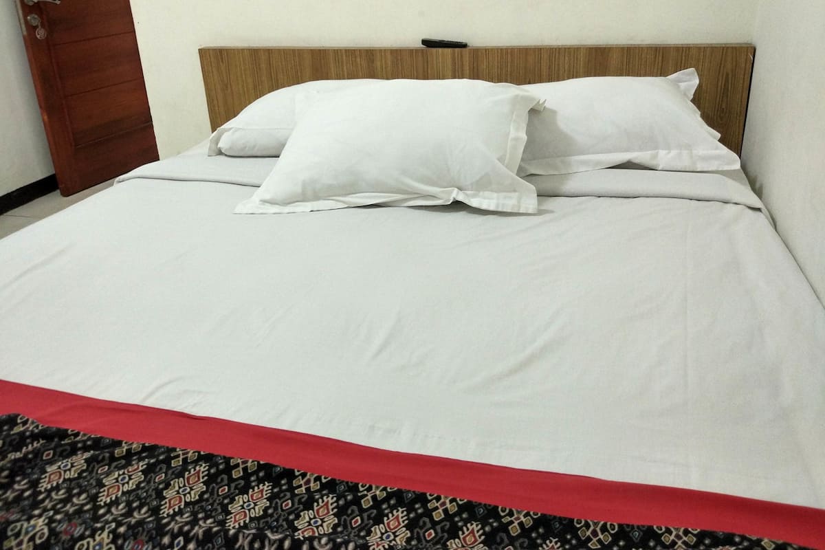 Un lit bien fait, avec une literie blanche et un couvre-lit rouge.
