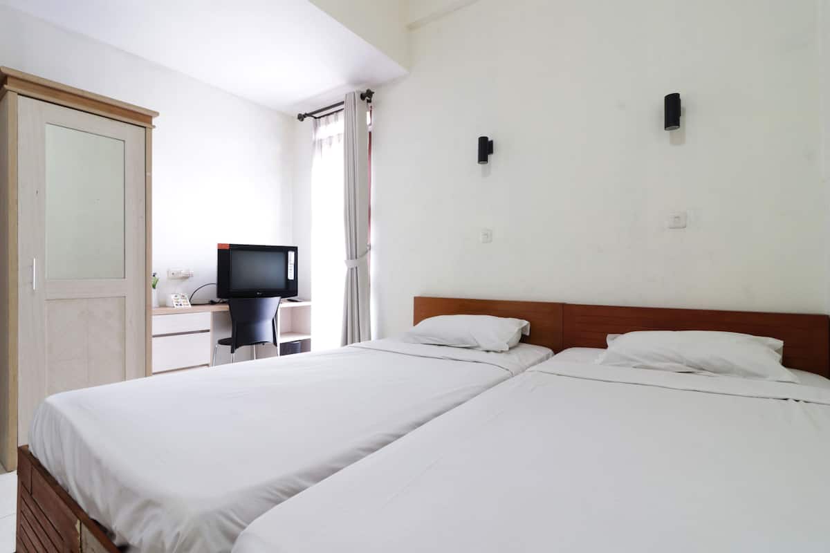 Une chambre d’hôtel avec deux lits, un bureau avec un ordinateur, une télévision et une armoire.