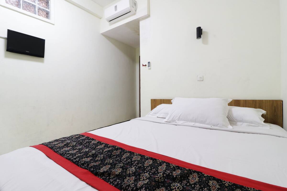 Une chambre d’hôtel équipée d’un lit, d’un climatiseur fixé au mur, d’une télévision et d’une porte avec un interrupteur pour la lumière.
